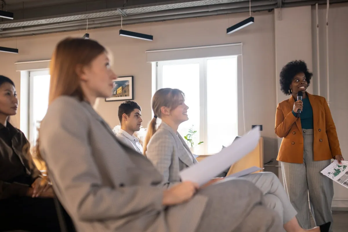 Une formatrice, micro à la main, anime une session devant un groupe d’adultes