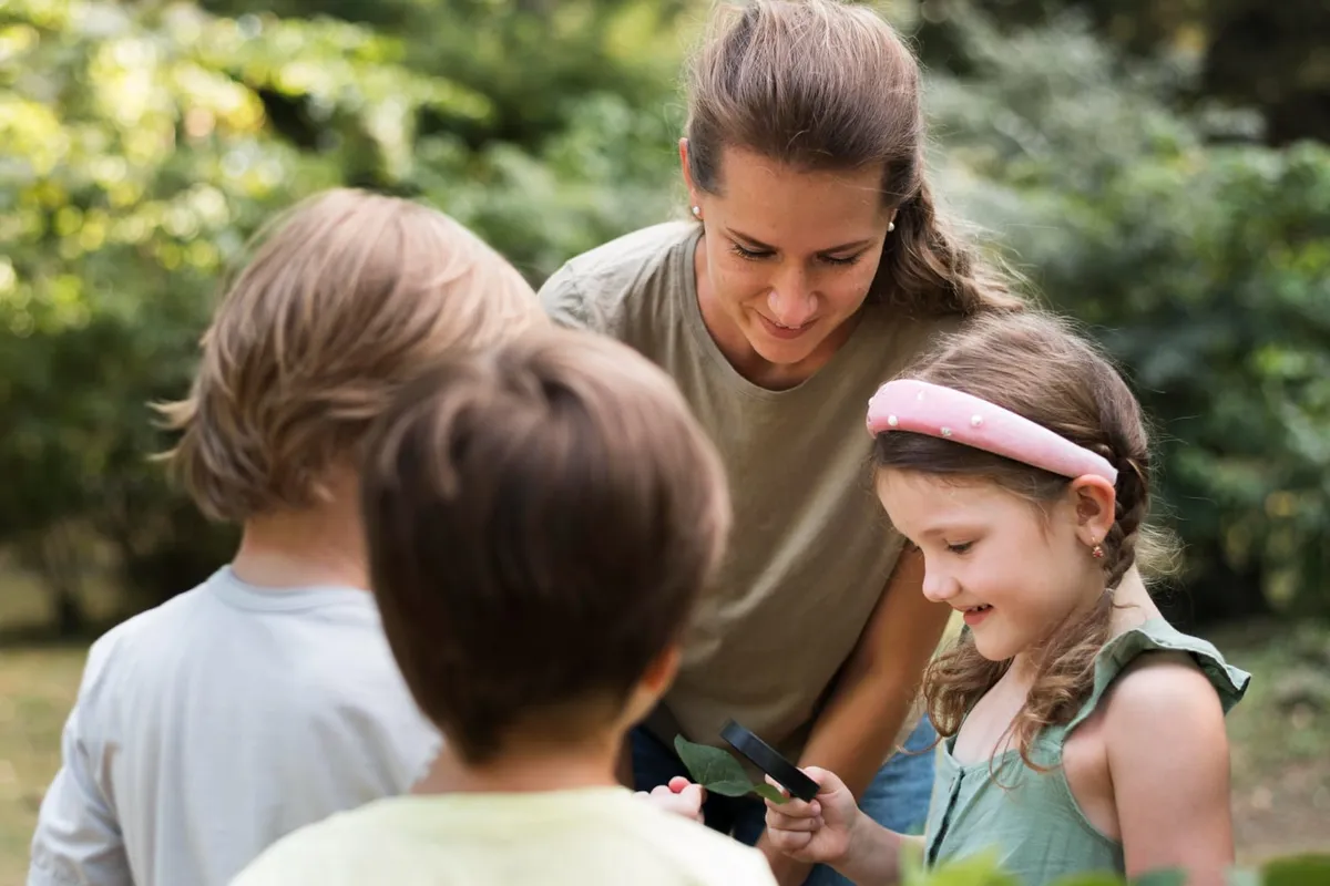 Une animatrice observe une feuille à la loupe avec des enfants, en plein air