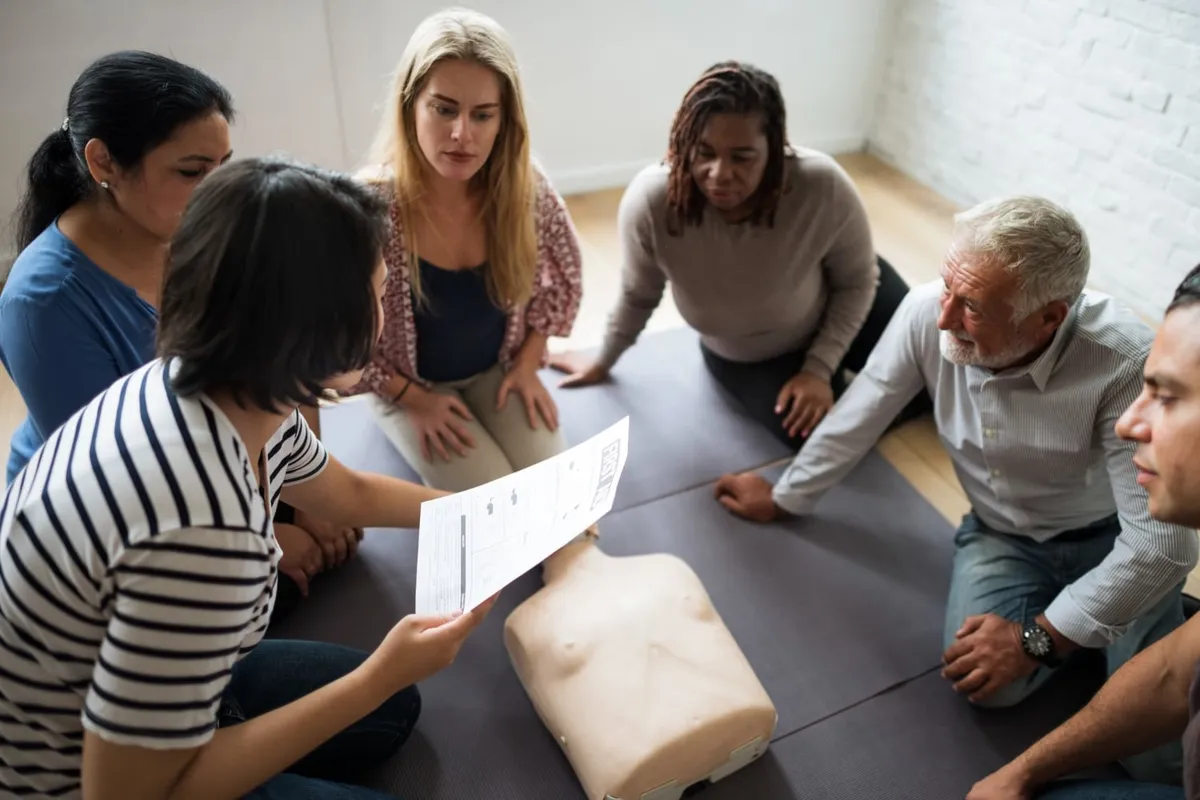 Des participants assis autour d’un mannequin de secourisme suivent une formation aux premiers secours