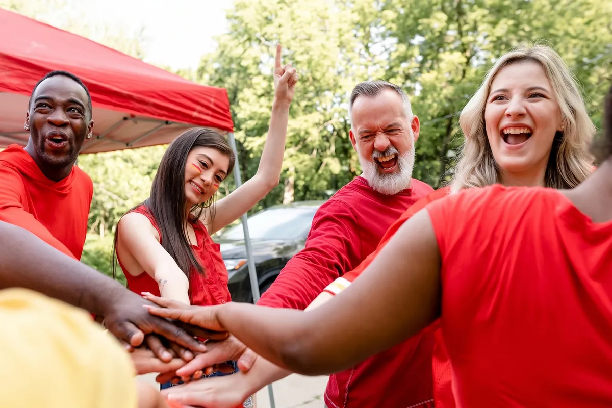 Une équipe en tee-shirts rouges joint les mains en riant lors d’une activité de cohésion en plein air